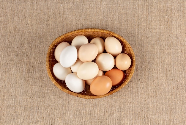 Farm chicken eggs different colors and sizes in wooden basket on natural coarse linen cloth