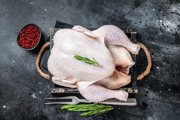 Farm Raw whole chicken in a wooden tray. Black background. Top view.