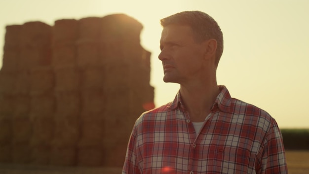 Farm worker golden sunlight at hay bales closeup Pensive man observing harvest