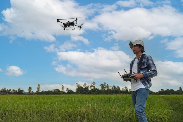 A farmer in a cap stands in a lush wheat field directing a drone that is flying above the edge Male controlling the equipment Farming technologies