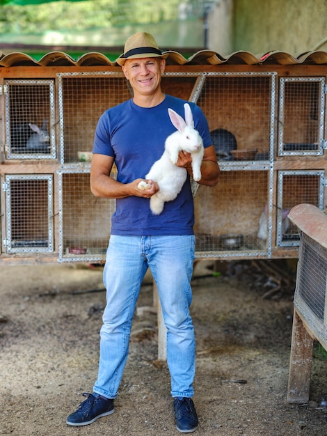 Farmer caucasian rural portrait in countryside with white rabbit in his arms outdoors outside