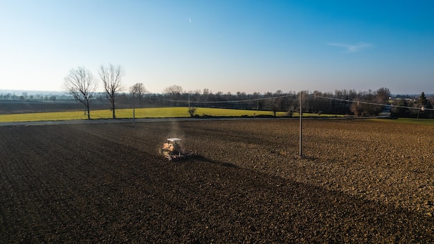 Farmer driving a crawler tractor ploughing and power harrowing surface crust breaking to facilitate the birth and seeding of plants on dry soil