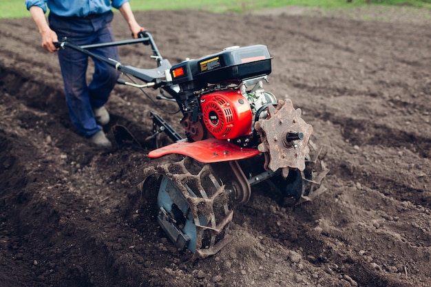 Farmer man driving small tractor for soil cultivation and potato planting