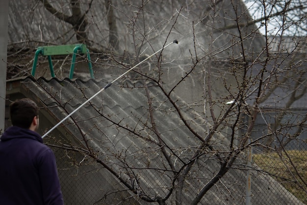 A farmer sprays a flowering fruit tree against plant diseases and pests