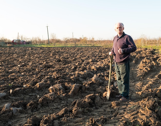 Farmer standing with a shovel on the field. Spring time. Beginning of spring work on the field