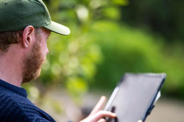 Photo farmer wearing a hat being sun smart using technology and a tablet and phone in a field studying a soil and plant sample in field