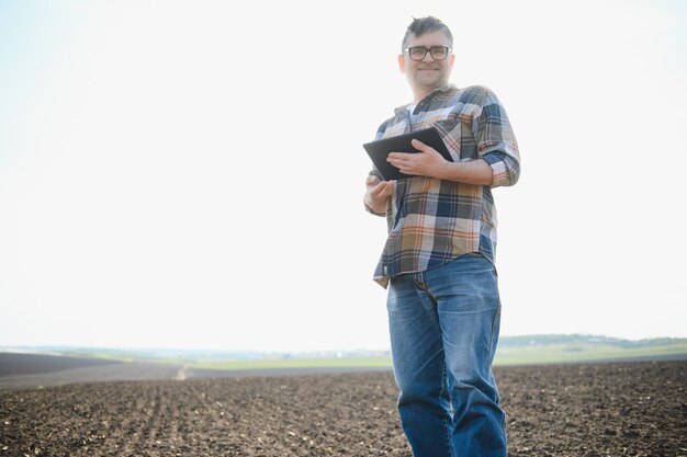 Farmer works in field in spring with tablet An elderly farmer looks at tablet and green shoots A smart agronomist with tablet in his hands checks field Environmentally friendly farming