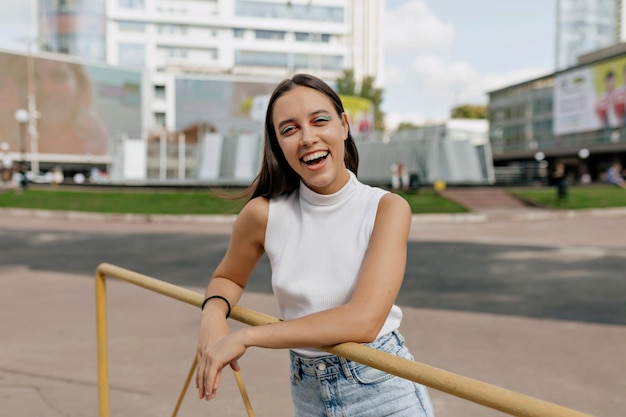 Fascinating adorable lady with happy smile and bright holiday make up is posing at camera in sunlight in the city