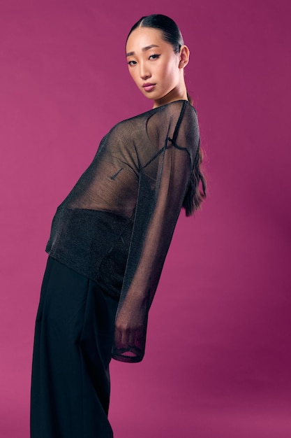 Photo fashion asian woman in black outfit posing against a purple background with hands on hips and head