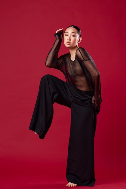 Photo fashion asian woman in black top and widelegged pants posing on red background with hands on hips