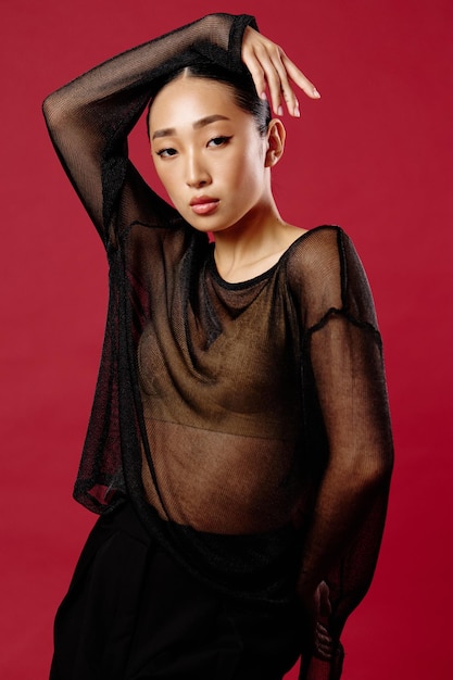 Fashion asian woman in a sheer top and black pants posing on a red background