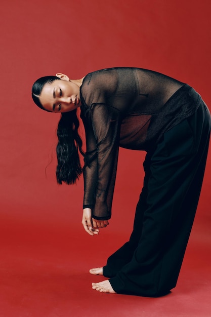 Photo fashion asian woman wearing a sheer top and black pants bending over on a red background with hands