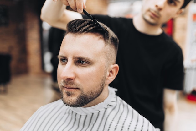 Fashion barber dressed in a black clothes tidies up men's beard and scissors it in the barbershop