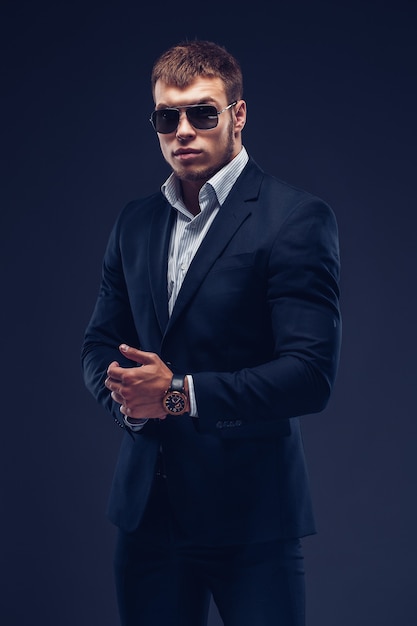 Fashion bearded young serious man in sunglasses luxury suit looking at camera on black 