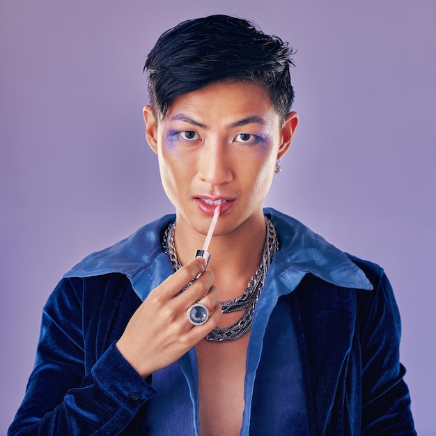 Fashion beauty and makeup with a man model in studio on a purple background applying red lipstick Face portrait and cosmetics with a young asian male indoors to promote a cosmetic product