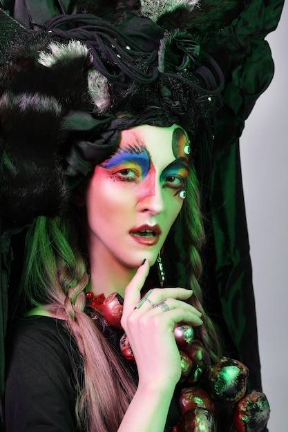 Fashion beauty people and halloween concept Young woman with a bright creative makeup and a big black headdress