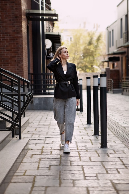 fashion blogger walking street wearing oversized black jacket grey jeans and trendy white sneakers