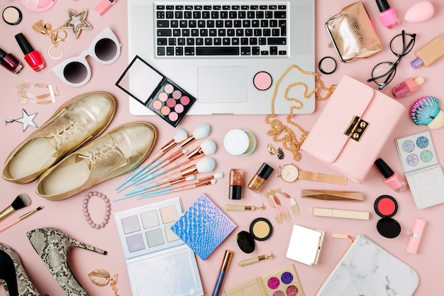 fashion blogger workspace with laptop and female accessory cosmetics products on pale pink table