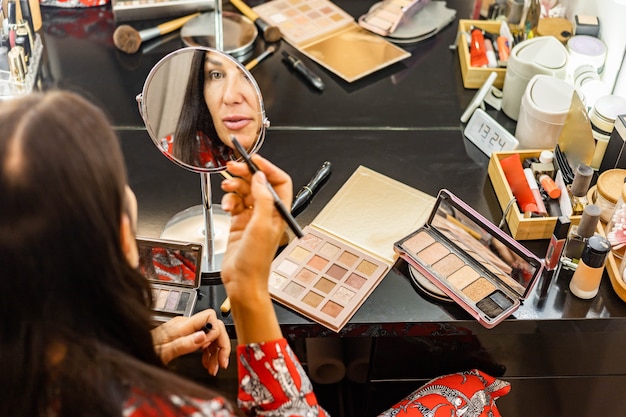 Fashion brunette woman getting ready to party event at home wardrobe makeup in front of mirror