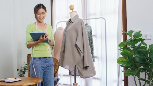 Fashion clothes online concept Female designer checks detail of clothes and taking notes on tablet