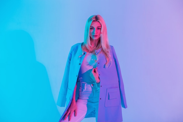 Fashion colored portrait of a beautiful elegant blonde girl in stylish business clothes look with a blue jacket on a neon pink light background