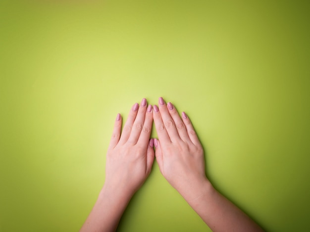 Fashion, female hands with manicure, nail care, healthy skin and natural cosmetics. Top view contrasting against a green background.