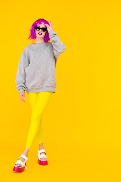 Fashion girl portrait on yellow background. Crazy style young woman in pink wig