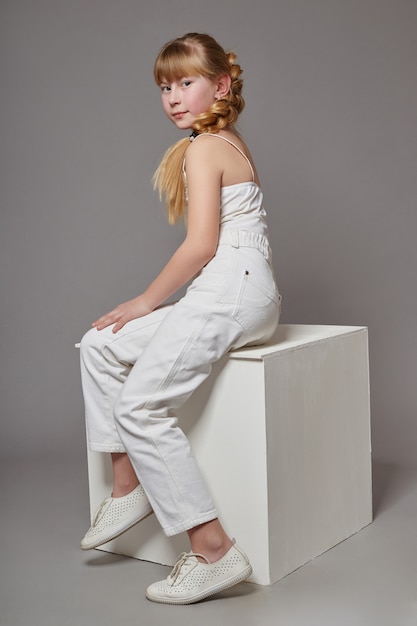 Fashion girl with long hair in casual clothes sitting on a white cube and posing