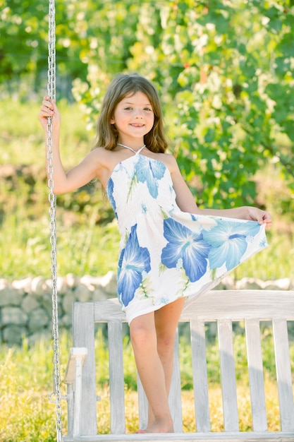 Fashion kids dress little child girl is swinging on a swing in summer park sunny joyful summer day c