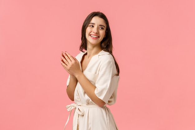 Fashion, leisure and beauty concept. Cheerful elegant and tender female tourist relaxing on spa resort, applying body lotion, hand cream, looking behind right side copy space, pink wall