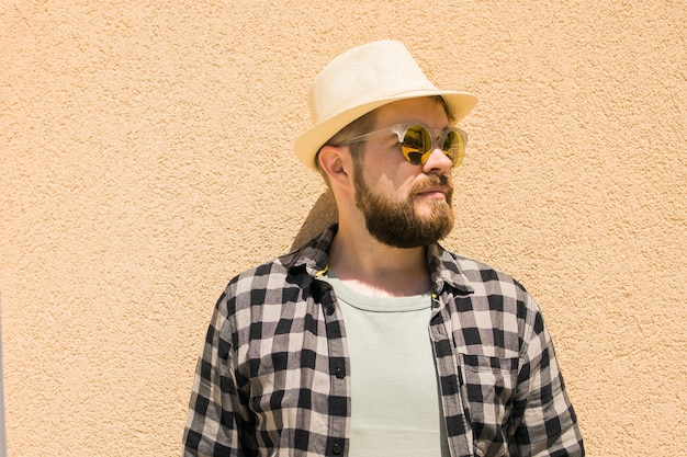 Fashion millennial stylish man posing on streets of european city Bearded handsome hipster man posing near wall with hard shadows on hot noonday copy space summer vacations and holiday concept