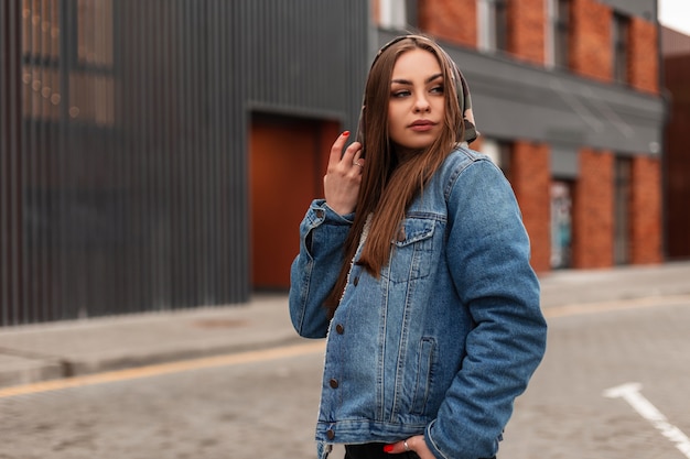 Fashion model american young pretty hipster woman in stylish denim jacket walks in the city. Fashionable urban girl in jeans clothes outdoors. Casual style. Youth street look. Spring wear for women.