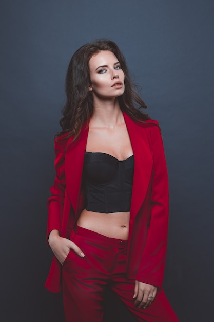 Fashion model in red suit. Young woman posing with red suit on gray