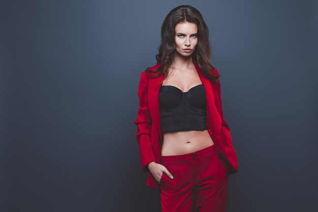 Fashion model in red suit. Young woman posing with red suit on gray