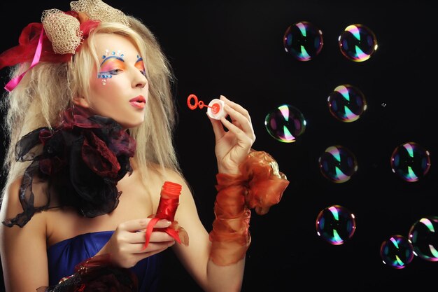 Fashion model with creative makeup blowing soap bubbles