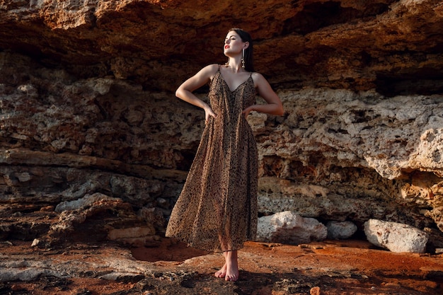 Fashion outdoor portrait of sexy beautiful elegant woman with long hair dressed in a luxurious evening dress posing on the summer beach