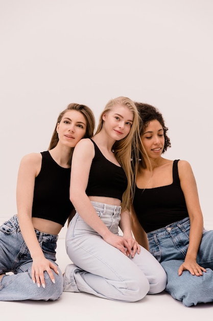 Fashion photo of three beautiful caucasian and afro women looking in different directions posing on white background Lifestyle beauty and multiracial friendship concept