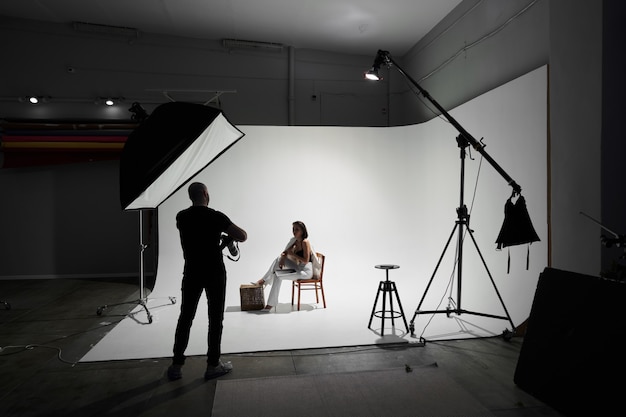 Fashion photography in a photo studio. Professional male photographer taking pictures of beautiful woman model on camera, backstage