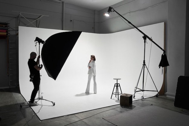 Fashion photography in a photo studio. Professional male photographer taking pictures of beautiful woman model on camera, backstage