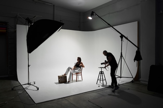 Fashion photography in a photo studio. Professional male photographer taking pictures of beautiful woman model on camera, backstage