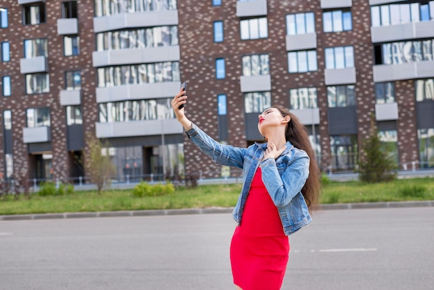 Fashion portrait of a beautiful girl in an elegant red dress with a summer dawn in the city