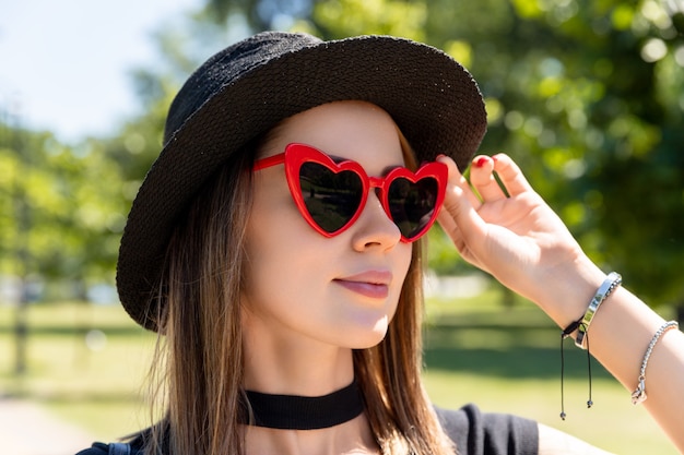 Fashion portrait of beautiful woman in black t-shirt and red skirt walking in the park. Trendy clothes glasses accessories. Shopping sale concept