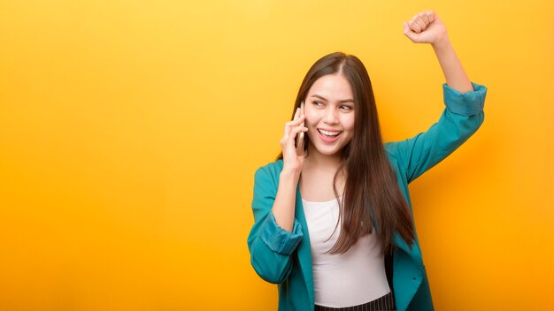 Fashion portrait of beautiful woman in green suit  using cellphone on yellow