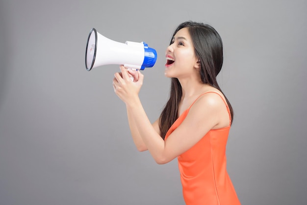 A fashion portrait of beautiful woman wearing orange dress is using megaphone