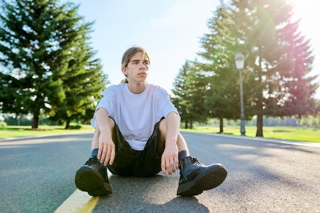 Fashion portrait of hipster teenager guy sitting on the road