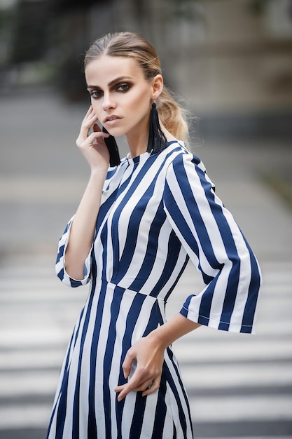 Fashion portrait of a pretty girl in a dress with a strip. Girl at the pedestrian crossing