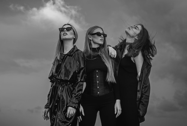 Fashion portrait of sexy group fashion models girls posing outdoor black style outfit against sky at