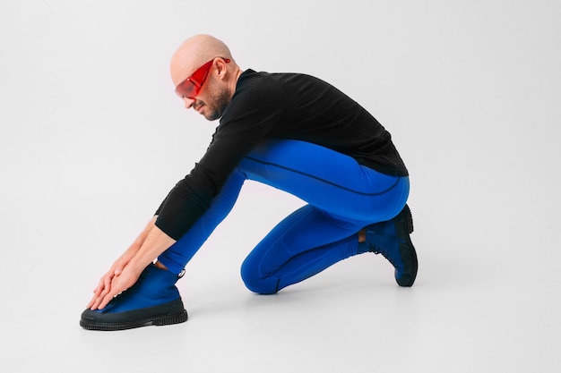 Photo fashion portrait of stylish man in blue tights and blue boots stretching and exercising.