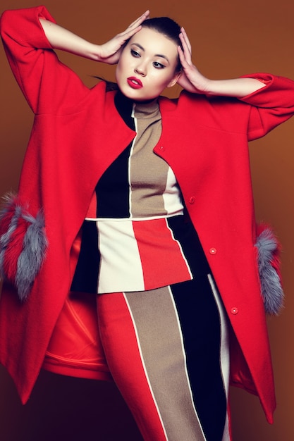 Fashion portrait of young asian woman in trendy skirt, top and red coat. .