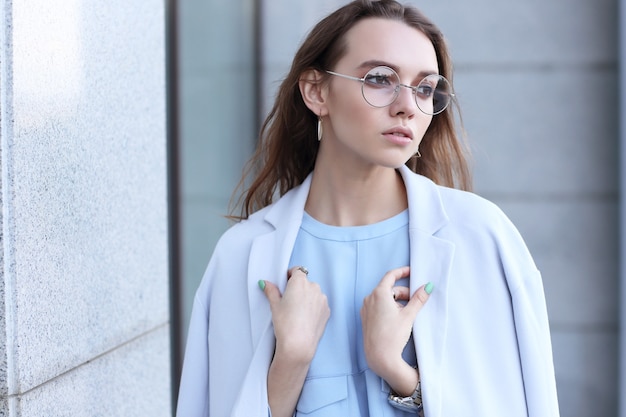 Fashion portrait of young elegant woman outdoor in jacket, dress, glasses. Trendy fashion look